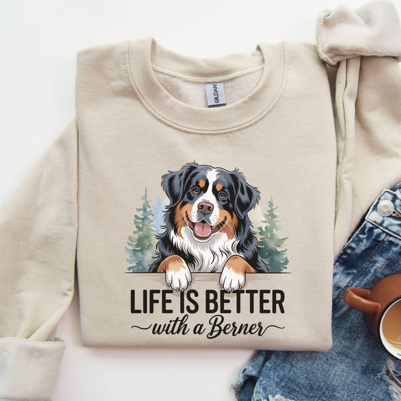 May include: A beige sweatshirt with a graphic of a Bernese Mountain Dog peeking over a sign that reads "Life is better with a Berner".