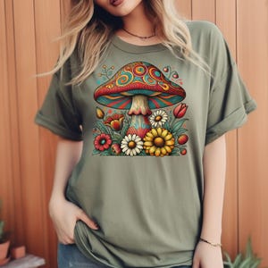 May include: A green t-shirt with a colorful mushroom and flowers graphic. The mushroom has red, yellow, blue, and green swirls. The flowers are red, yellow, and white.