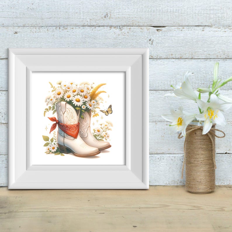 May include: A framed watercolour print showing white cowboy boots filled with daisies and wheat. A red bandana is tied around one boot. A yellow butterfly and other wildflowers are also present. The print is displayed on a wooden surface.
