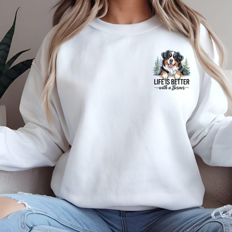 May include: White sweatshirt with a pocket featuring a Bernese Mountain Dog peeking out and the text "Life is better with a Berner".