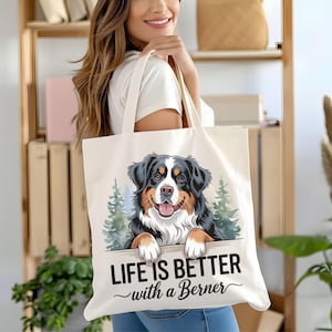 May include: White canvas tote bag with a cartoon illustration of a Bernese Mountain Dog peeking over a wooden sign. The sign reads "Life is better with a Berner".
