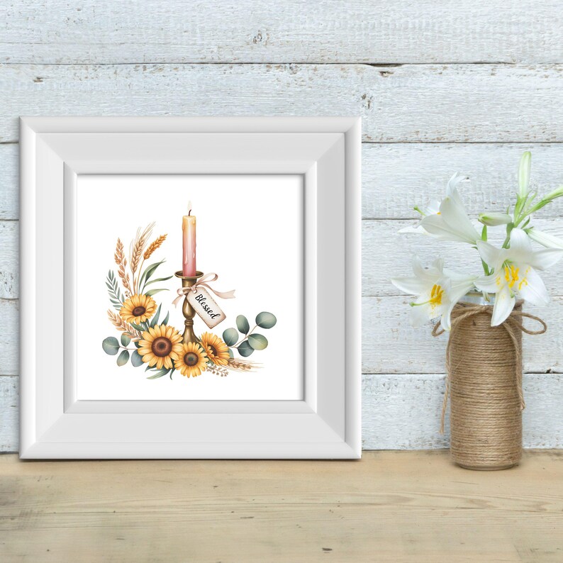 Op de afbeelding: Een ingelijste aquarelprint met een kaars in een gouden kandelaar, omringd door zonnebloemen, tarwe en groen. Een label met de tekst "Blessed" hangt aan de kandelaar. De print zit in een witte lijst, met rechts een vaas met witte bloemen.