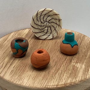 May include: A collection of miniature terracotta pottery and a woven basket. The pottery includes small vases with turquoise and orange accents, and a round, open-topped vessel. The basket is circular with a spiral design.
