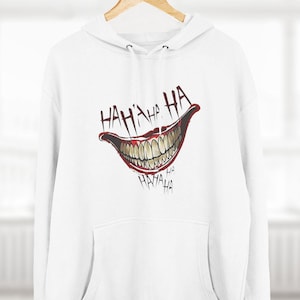 May include: White hoodie with a large graphic of a grinning mouth with the words "HA HA HA" in red. The hoodie has a front pocket and a drawstring hood. The design is centered on the chest.