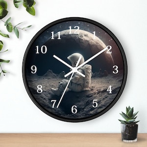 May include: Black round wall clock with white numbers and hands. The clock face features a space scene with an astronaut sitting on the moon.