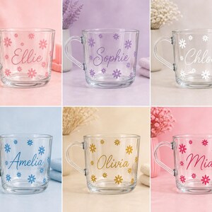 May include: A collection of six clear glass mugs, each featuring a unique name in cursive script surrounded by small flower decals. The names include Ellie in pink, Sophie in purple, Chloe in white, Amelia in blue, Olivia in gold, and Mia in magenta.