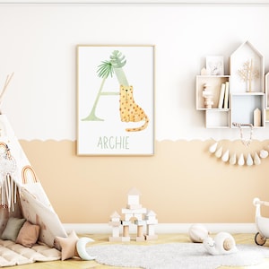 May include: A framed watercolor print featuring the letter "A" with a leopard illustration and the name "Archie" in green text. The artwork is displayed in a child's room with a teepee, shelves, and toys.