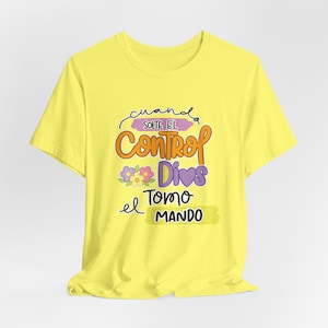 May include: A bright yellow short-sleeve t-shirt featuring a graphic print with the text "cuando SOLTE EL Control Dios Tomo el MANDO". The design includes colorful floral accents, a purple heart, and various decorative shapes in orange and purple.