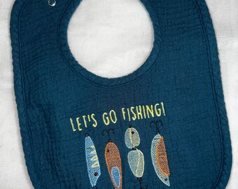 May include: A dark blue baby bib with the text "Let's go fishing!" embroidered on it. The bib has four embroidered fishing lures in yellow, orange, and blue.
