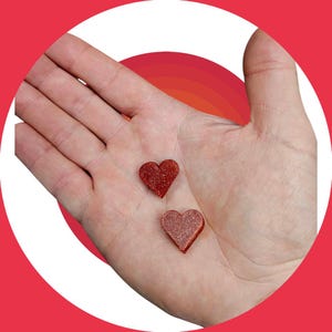 May include: Two red glitter heart-shaped ornaments in the palm of a hand.
