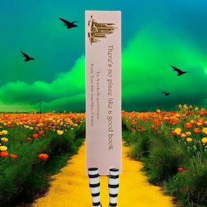 May include: A pink bookmark with black and white striped legs. The bookmark has the text "There's no place like a good book." and "Toc A wickedly good Grama" and "From: Your little munchkin, Carmen". The bookmark is standing on a yellow brick road in a field of yellow and orange flowers.