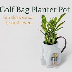 May include: A white golf bag planter pot with a brown handle, holding a green plant with yellow spots. The planter has two golf tees in a holder. Text on the image reads "Golf Bag Planter Pot" and "Fun desk decor for golf lovers."