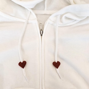 May include: White zippered hoodie with a brown heart detail on each drawstring.
