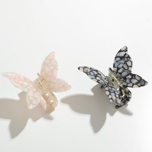 May include: Two butterfly-shaped hair clips. One is pink and white with a mottled pattern, the other is black and white with a mottled pattern.