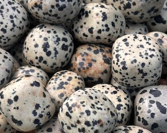 May include: A collection of smooth, rounded stones with a speckled pattern. The stones are primarily off-white with black and brown spots, creating a dalmatian-like appearance. The stones vary in size and shape, filling the frame.