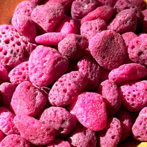 May include: A close-up shot of a collection of pink, porous, irregularly shaped stones. The stones vary in size and have a rough, textured surface. The color is a vibrant, saturated pink, with some stones appearing slightly darker.