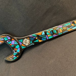 May include: A decorative wrench with a colorful stained-glass design. The wrench is black with geometric shapes in teal, purple, orange, and yellow. The number "60" is visible on the wrench.