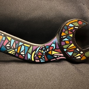 May include: A black wrench painted with a colorful stained glass design. The wrench has a geometric pattern with shades of blue, green, yellow, pink, and purple.