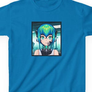May include: A bright blue short-sleeved t-shirt featuring a centered rectangular graphic print of an anime-style character with vibrant teal hair, large eyes, and a headset, set against a blurred background within a black frame border.