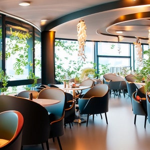 May include: A modern restaurant interior with large windows, blue and gray chairs, and white tables. The restaurant has a minimalist design with a focus on natural light and greenery.