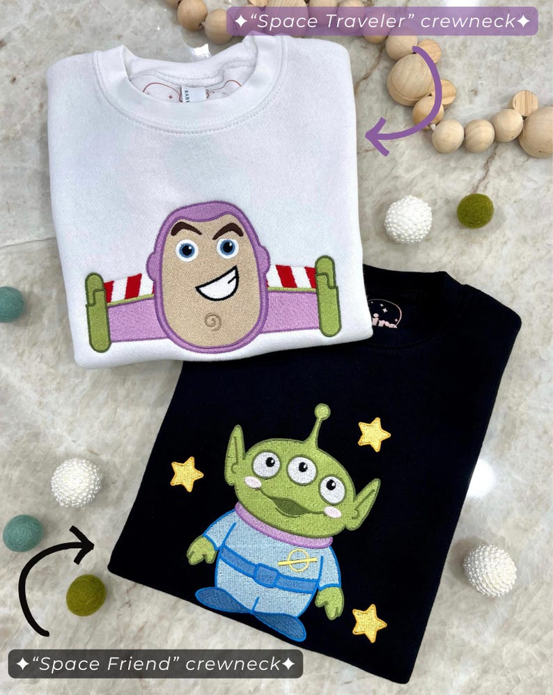K&ouml;nnte beinhalten: Zwei Sweatshirts mit Rundhalsausschnitt, eines wei&szlig; und eines schwarz. Das wei&szlig;e Sweatshirt zeigt ein Buzz Lightyear-Design, w&auml;hrend das schwarze einen gr&uuml;nen Au&szlig;erirdischen mit gelben Sternen zeigt. Die Sweatshirts sind Teil der Kollektion "Space Traveler" und "Space Friend".