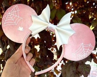 May include: Pink velvet Minnie Mouse ears with a white bow and a spider web design. The ears have a white spider and web design.