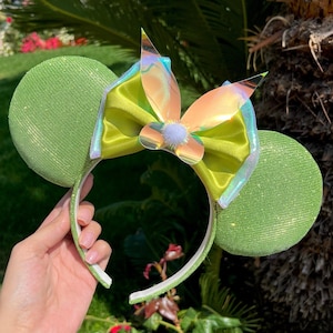 Op de afbeelding: Groene glitter muis oren met een grote groene satijnen strik en een iriserende vlinder accent.