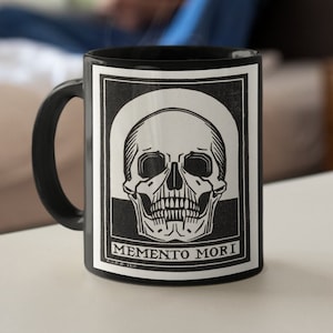 May include: Black coffee mug with a white skull and bones graphic and the text "Memento Mori".