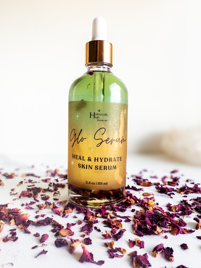 May include: A glass bottle of green serum with a gold lid and dropper. The bottle is labeled "Glo Serum Heal & Hydrate Skin Serum 3.4 oz / 101 ml" and is surrounded by rose petals.
