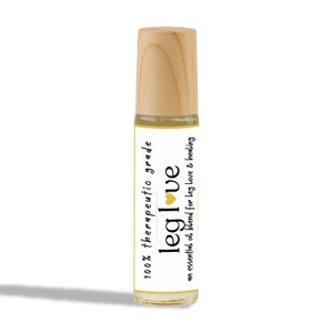 Puede incluir: Una pequeña botella de vidrio con una tapa de madera y una etiqueta blanca. La etiqueta dice "100% therapeutic grade leg love" con un pequeño corazón amarillo. La botella contiene un líquido transparente.