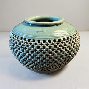 May include: A light green ceramic vase with a lattice design. The vase has a round body and a wide opening.