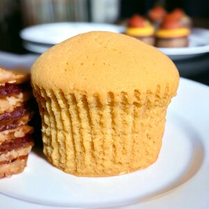 Peut inclure: Un cupcake doré avec un dessus lisse légèrement bombé et un bord cannelé. Le cupcake est posé sur une assiette blanche.