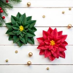 May include: Two poinsettia flowers, one green and one red, with yellow centres, are displayed on a white wooden surface. Gold baubles and sprigs of greenery are scattered around the flowers, creating a festive holiday scene.