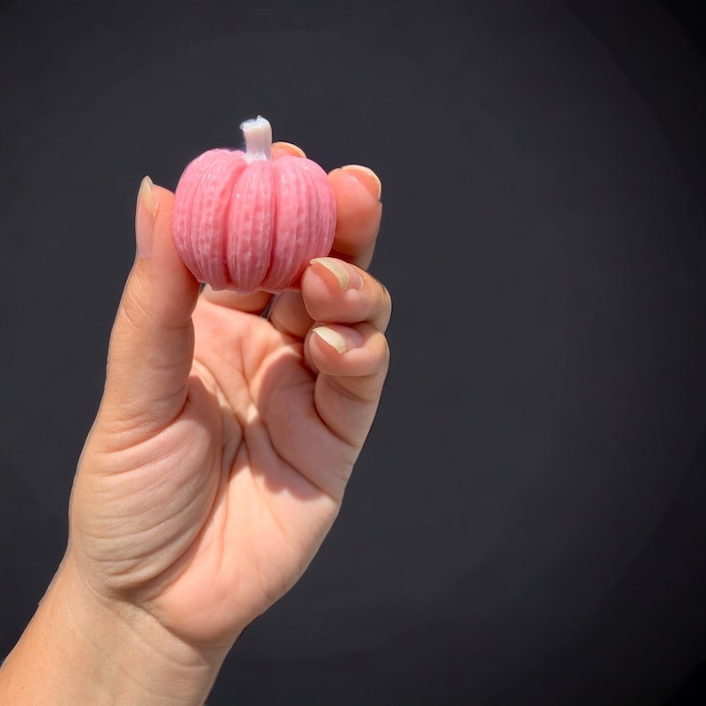 May include: A pink pumpkin-shaped candle with a white wick.