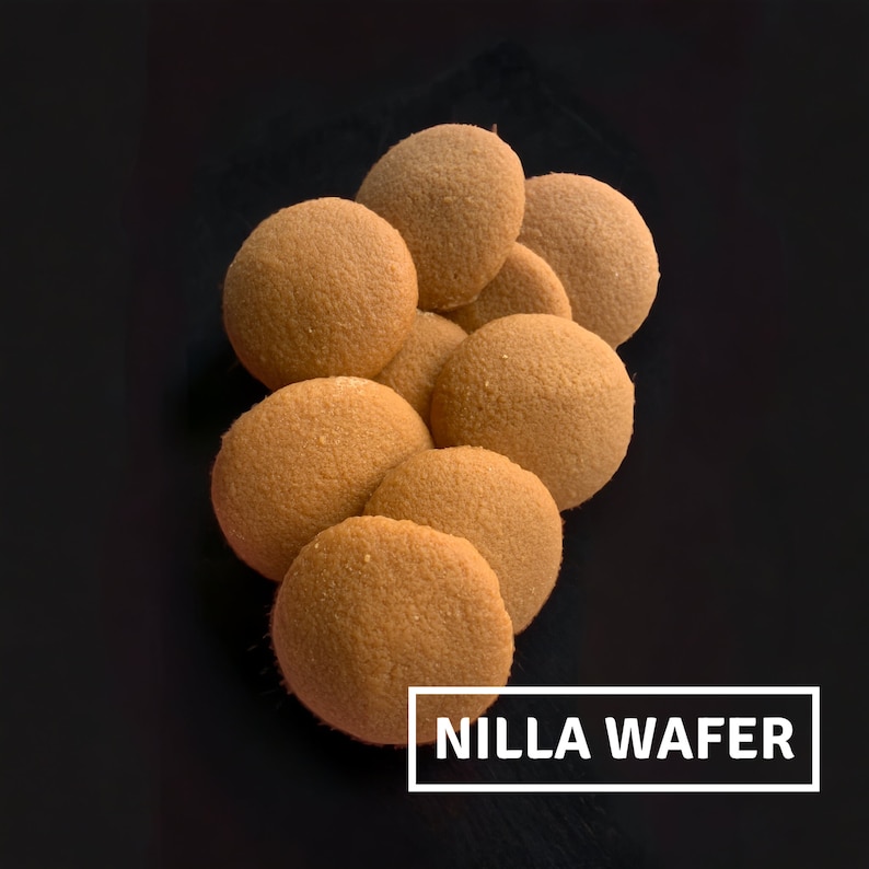 May include: A close-up of a pile of round, light brown Nilla wafer cookies on a black surface. The text "NILLA WAFER" is printed in white on a black rectangle.