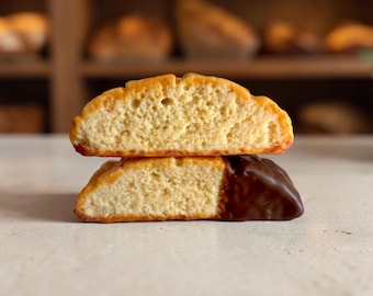 May include: Two halves of a golden-brown baked cookie stacked vertically. The top half shows a porous, light-colored interior texture. The bottom half features a smooth, dark brown chocolate coating covering one side of the cookie.
