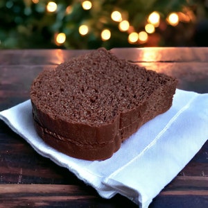 May include: A slice of chocolate bread on a white napkin. The bread is dark brown and has a slightly crumbly texture.