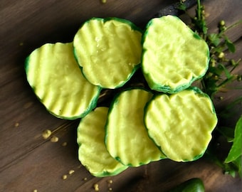 May include: Five round, crinkle-cut pickle slices with a pale yellow-green color and textured, wavy edges. The slices are arranged in a cluster, showing a firm, matte surface with subtle variations in tone across each individual piece.