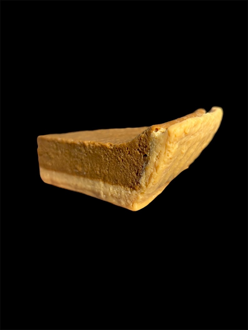 May include: A single slice of pie with a light brown top layer, a darker brown middle layer, and a light-colored bottom layer. The pie slice has a slightly uneven shape and is set against a black background.