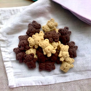 Pode incluir: Um monte de biscoitos em forma de urso castanho e bege num pano branco.