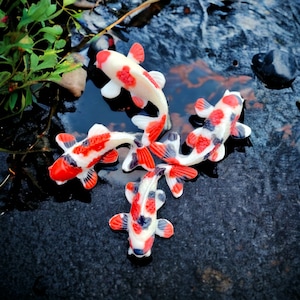 May include: Five colorful koi fish with red, white, and black markings are arranged in a star shape on a dark gray background. The fish are made of a smooth, shiny material and appear to be floating in water.