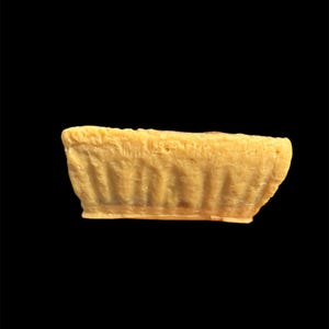 May include: A small, rectangular, light yellow object with a textured surface. The object has a slightly curved shape and appears to be made of a solid material. The background is solid black.