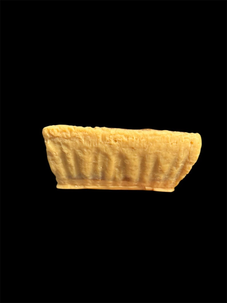May include: A small, rectangular, light yellow object with a textured surface. The object has a slightly curved shape and appears to be made of a solid material. The background is solid black.