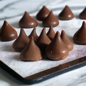 Op de afbeelding: Een close-up van een bakplaat bekleed met bakpapier en gevuld met chocolade kusjes. De kusjes zijn in een verspringend patroon gerangschikt, waarbij sommige elkaar overlappen.
