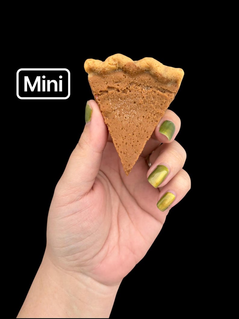 May include: A mini, triangular-shaped pastry with a light brown color and a wavy crust. The word "Mini" is displayed in a white box with a black background. The pastry is held against a black background.