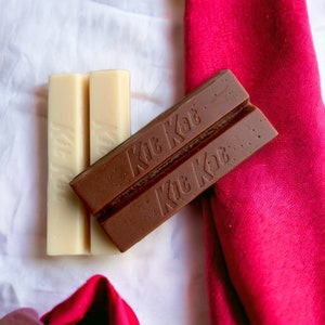May include: Two white chocolate bars with the text "Kit Kat" printed on them, next to two brown chocolate bars with the text "Kit Kat" printed on them.