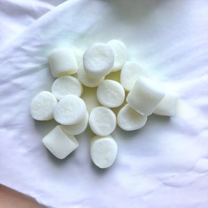 May include: A pile of white round wax melts, arranged on a white surface.