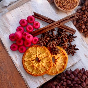 May include: A close-up of a wooden tray with dried orange slices, star anise, cinnamon sticks, and pink and red berries. The tray is on a wooden surface.
