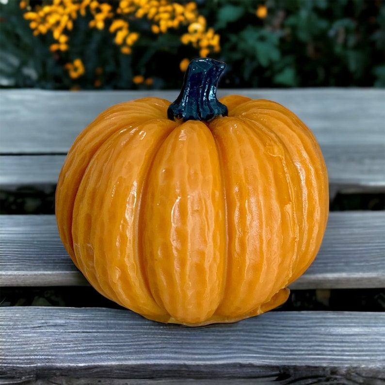 May include: A small, orange pumpkin with a dark blue stem. The pumpkin has a smooth, slightly shiny surface and is sitting on a gray wooden surface.