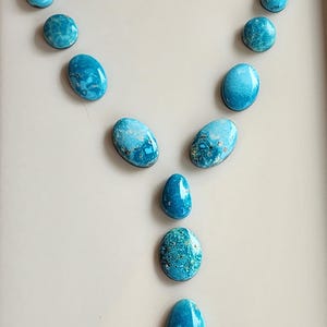 May include: An arrangement of turquoise gemstones in various shapes, including teardrops and ovals. The stones display a vibrant blue hue with natural matrix patterns, set against a neutral background. The gemstones are likely for jewelry making.